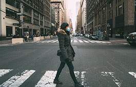 A woman crossing a wide New York street wearing a mask 
